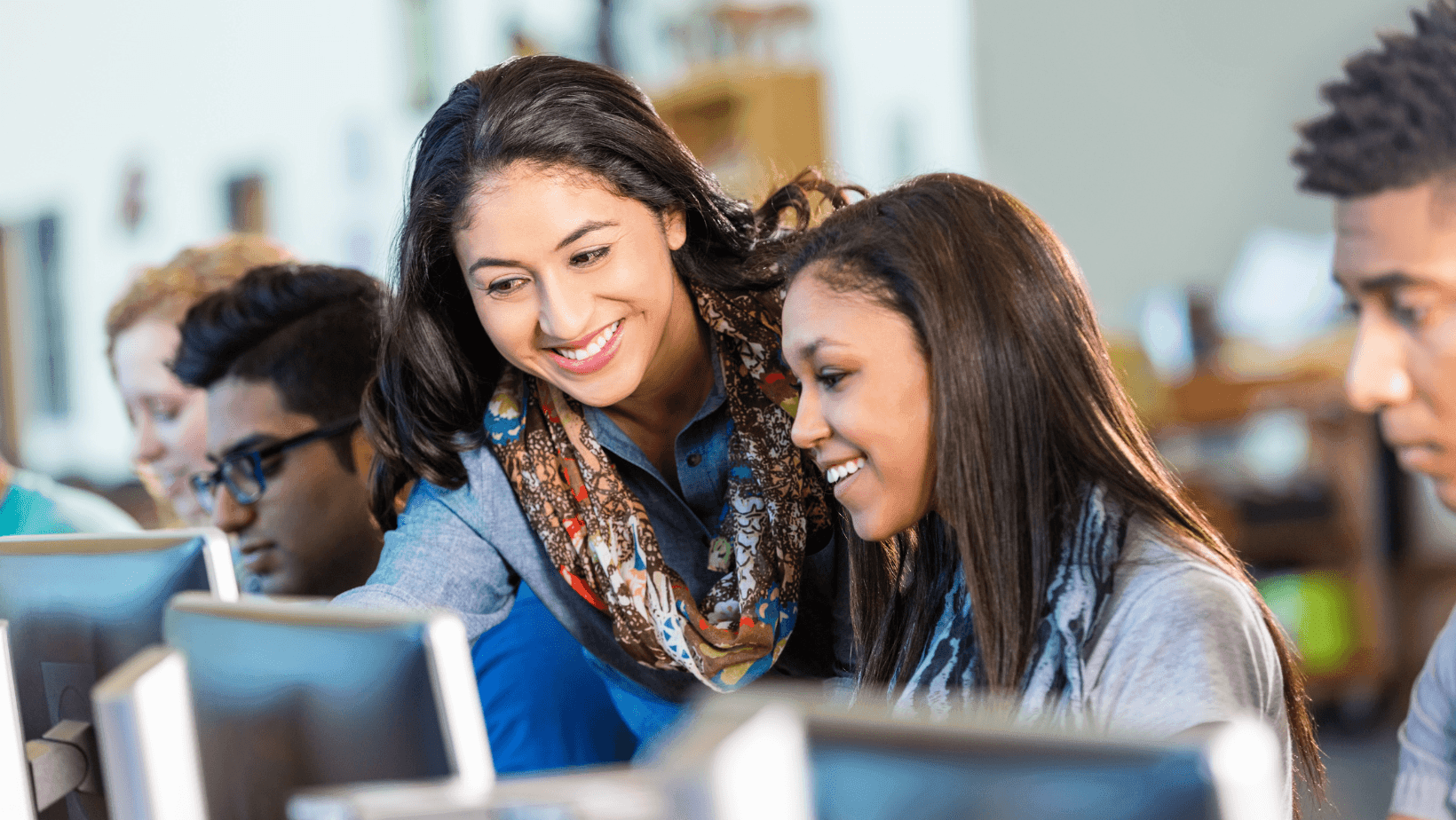 teacher or tutor helping students in computer lab classroom