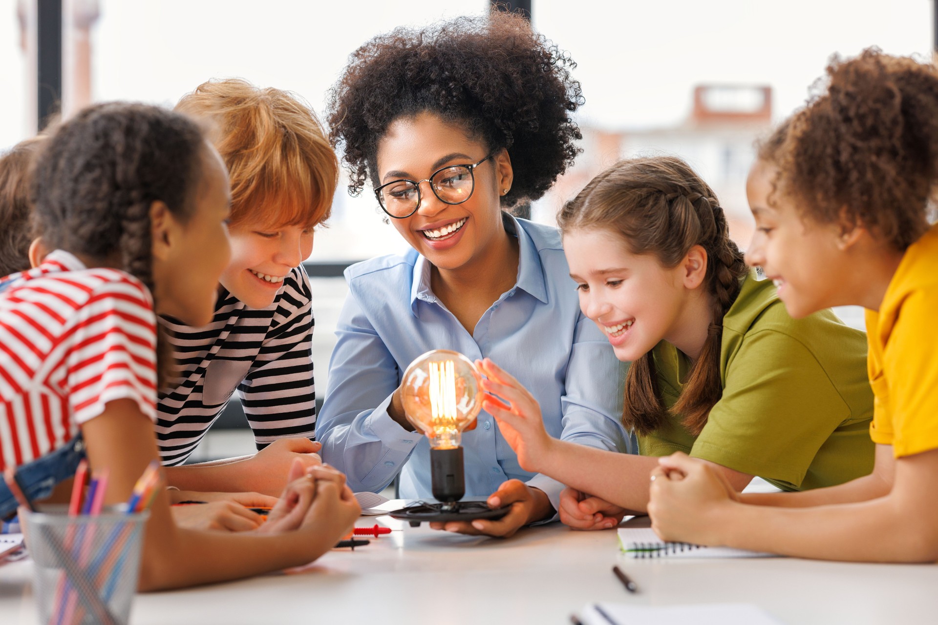 Multiethnic teacher and kids studying electricity and incandescent light bulb at physics lesson