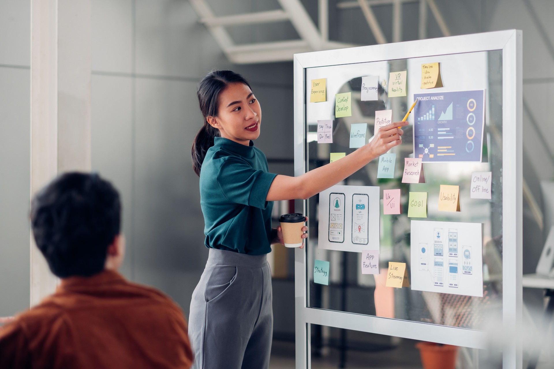 asian change management practitioner presenting mobile app interface design on whiteboard in meeting at modern office. Research based transformation